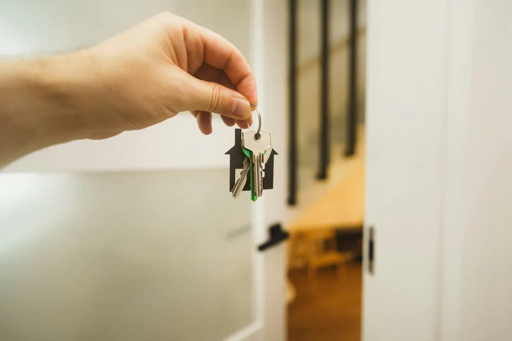 A hand holding a set of house keys in front of an open door