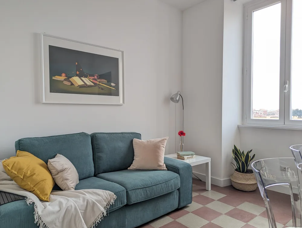 Soggiorno con divano e poltrona accanto alle alte finestre all’Ostiense 353 Apartment